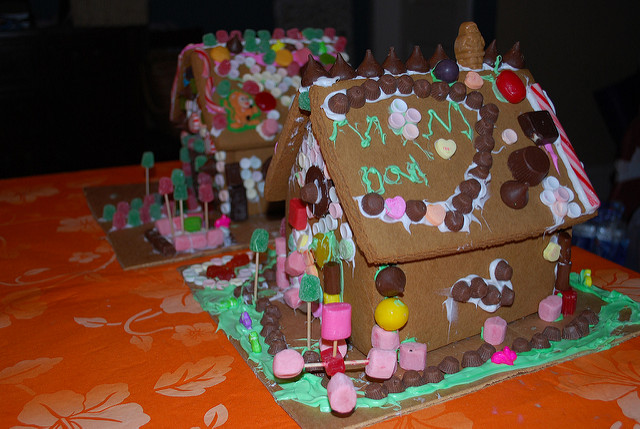 Two gingerbread houses, each covered in candy, stand side by side on an orange tablecloth.
