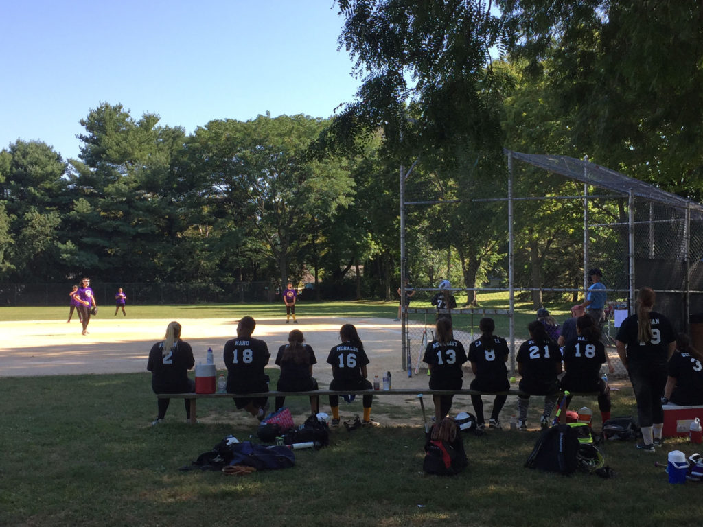 A girls' softball team watches while one of their teammate's bats.