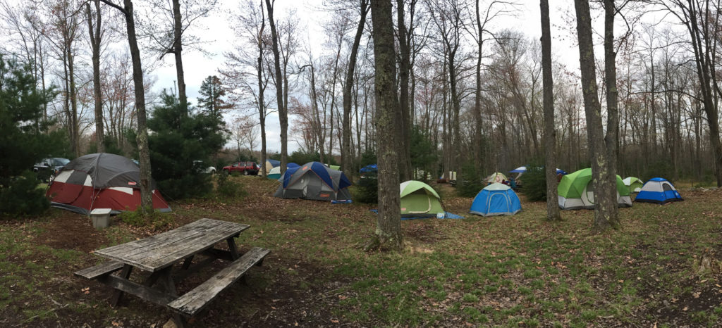 Several tents dot a campsite in early spring. A picnic table can be seen in the foreground.