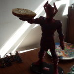 A large plastic super villain figure holds a bagel.