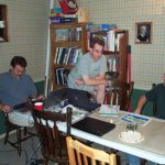 Three gamers sit at a gaming table, discussing the game.