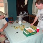 Two male gamers play a tile-based board game.