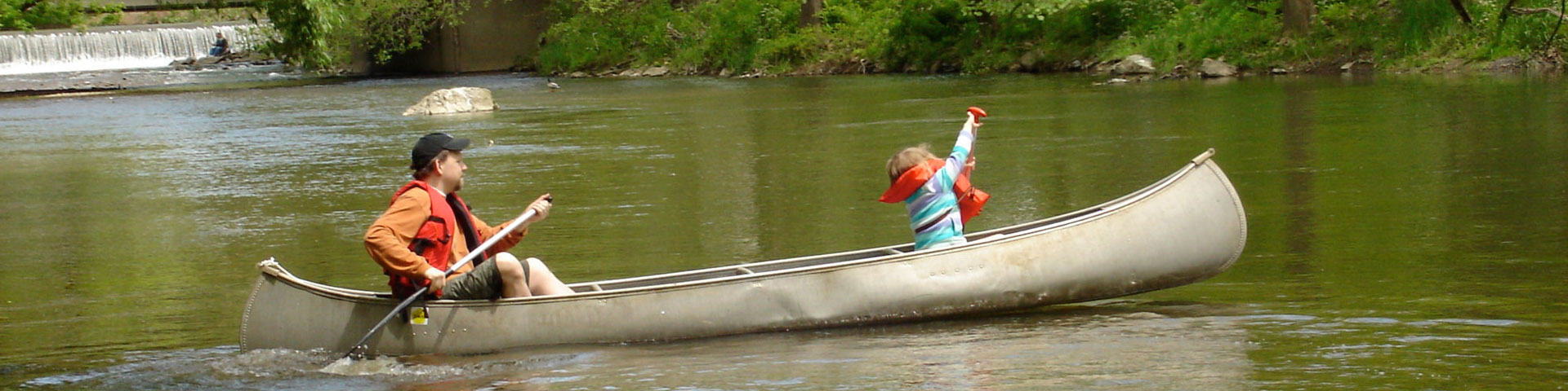 An adult male and a young girl paddle in a canoe on a creek.
