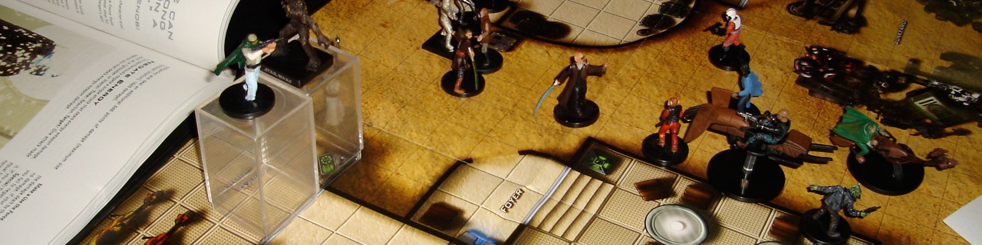 Star Wars-themed miniatures face off on a desert-colored battle map. A Saga Edition rulebook appears to the lefthand side.