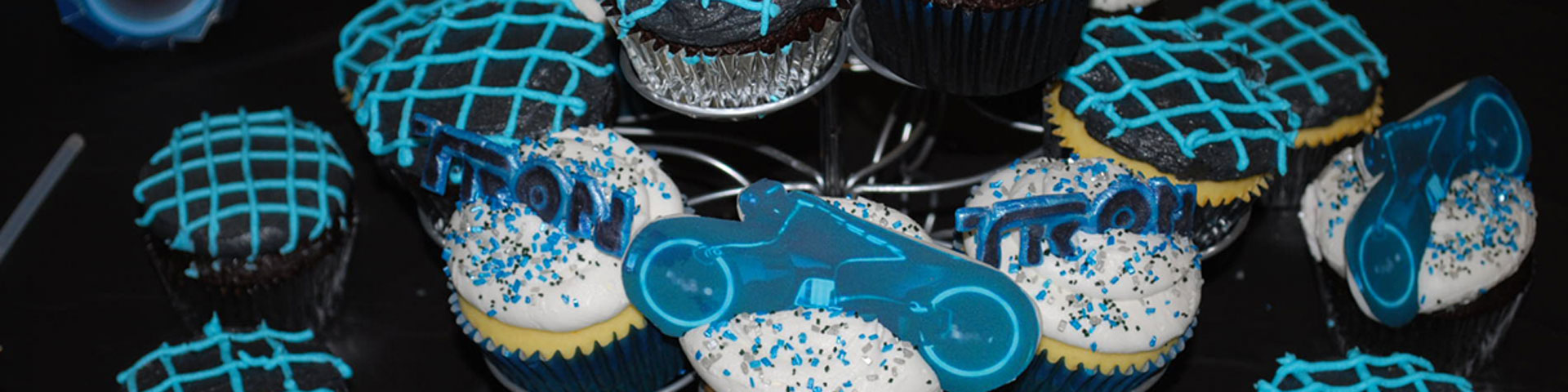 A pyramid of chocolate and vanilla cupcakes decorated with blue grids. Some of the cupcakes have lightcycles and other items from Tron on them.