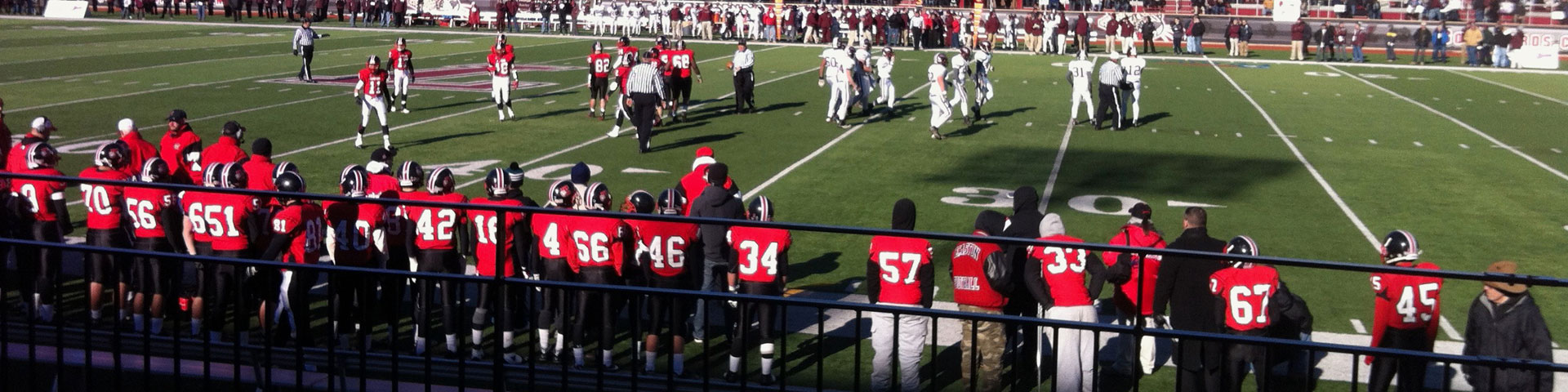 Red-jerseyed high school football players line the sidelines.