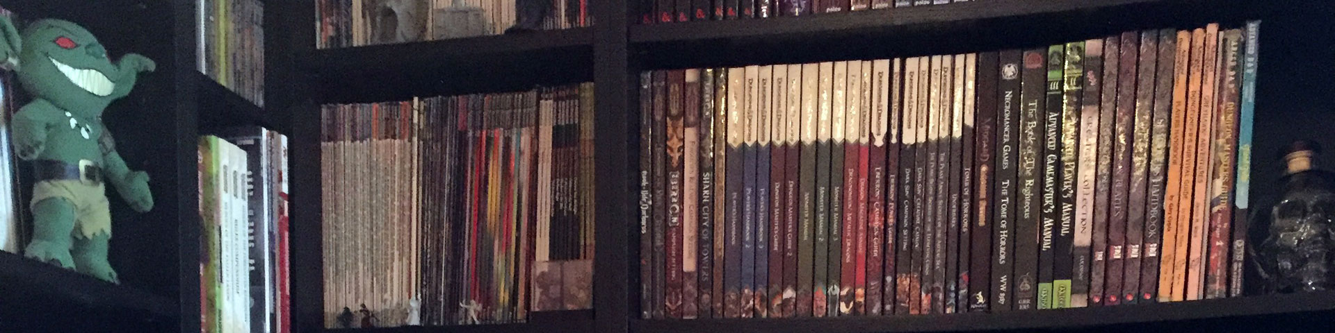 A variety of role-playing games (and one Pathfinder goblin) stand on a black bookshelf.
