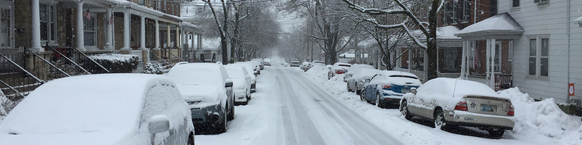 A snow-covered city street lined with cars.