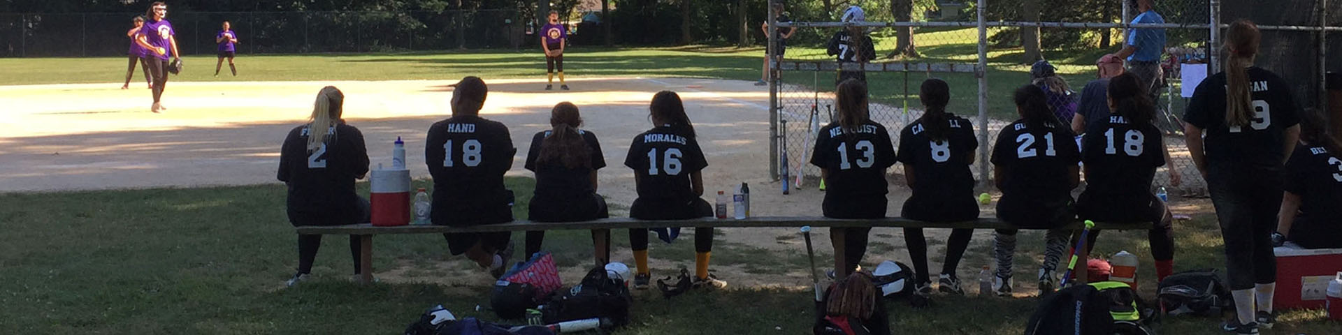 Girls in softball uniforms sitting on a bench.