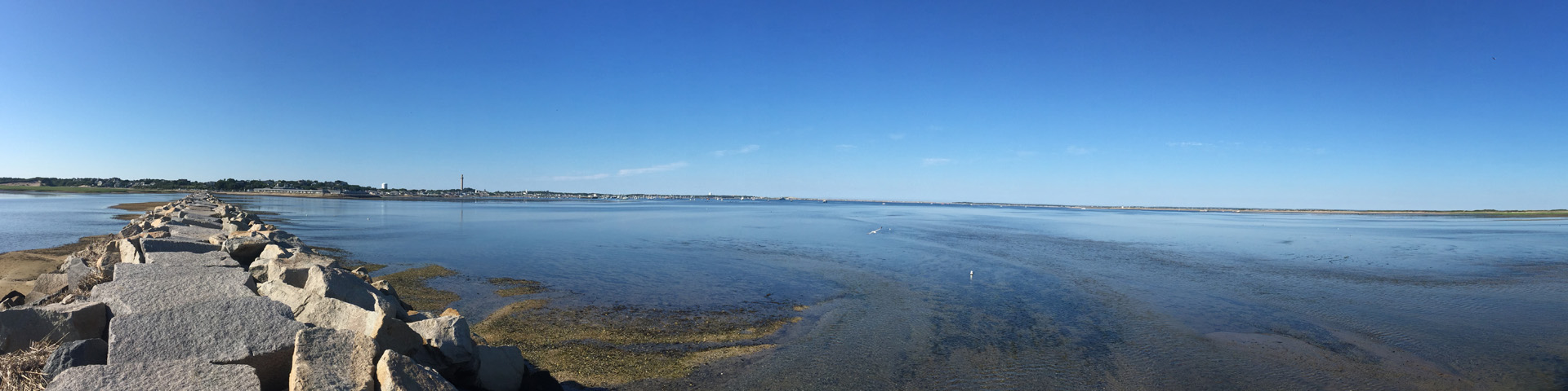 A breakwater comprised of large rocks stands on the left side of the screen; to the right is the bay.