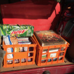 Two orange milk crates filled with role-playing game books, board games, and a case of Mountain Dew soda.