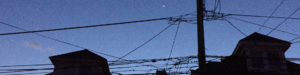 A bright planet - Venus -- appears against a darkening blue sky. Shadowed buildings and phone lines appear in the foreground.