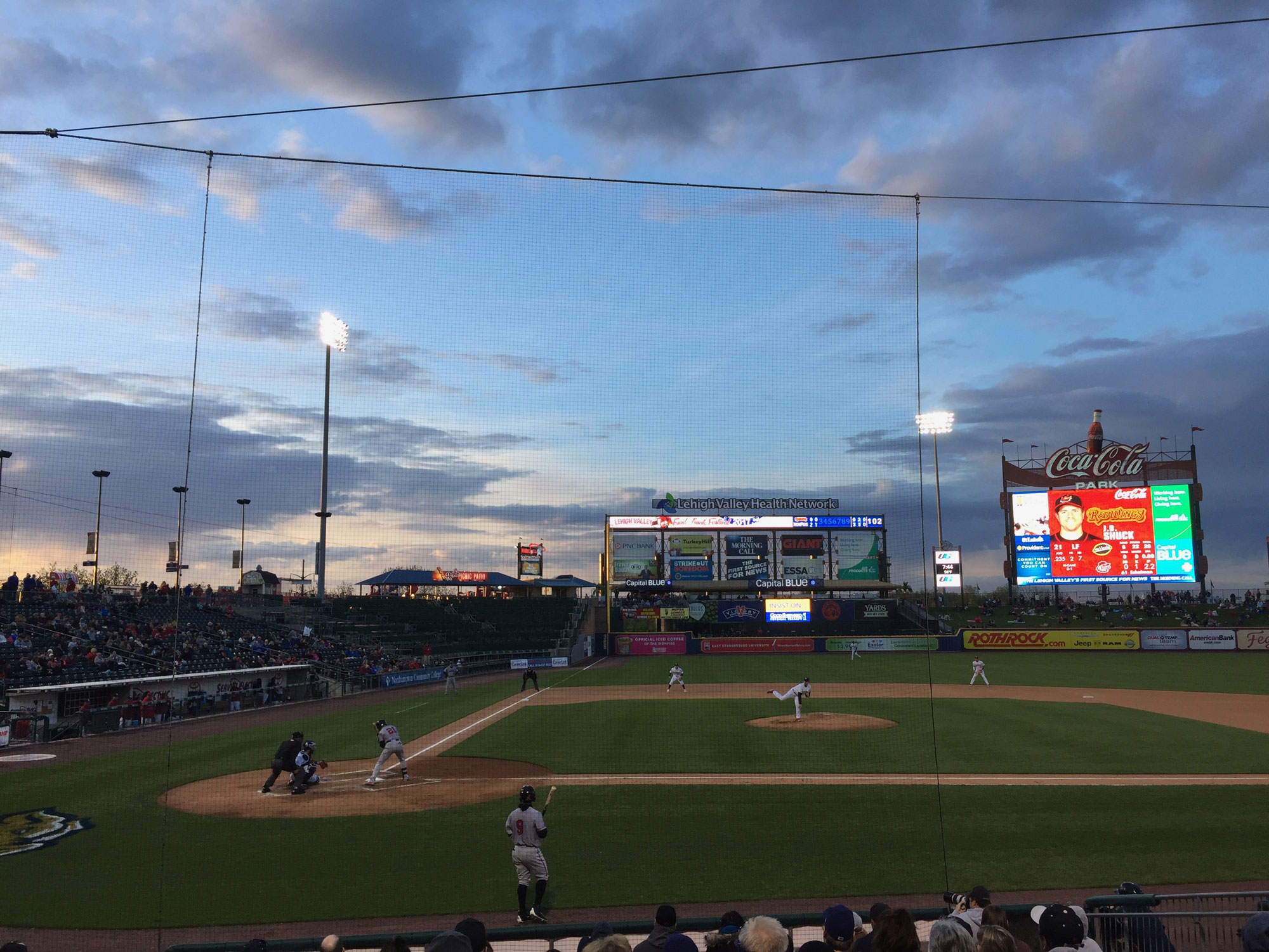 A minor league baseball park at sunset. The mostly blue sky is punctuated with clouds shading darker as the sun goes down.