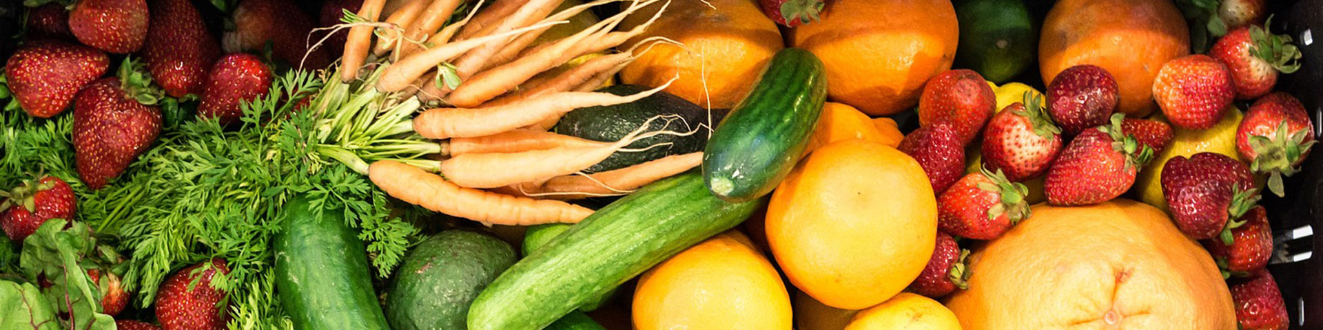 An assortment of vegetables and fruit including carrots, squash, oranges, and strawberries.