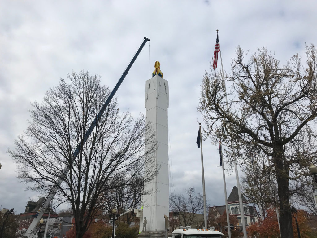 A crane puts the final touches on the Peace Candle in Easton's Centre Square. The candle is taller than the nearby flag poles and trees.