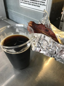 A cup of brown ale and a piece of bacon in aluminum foil. 