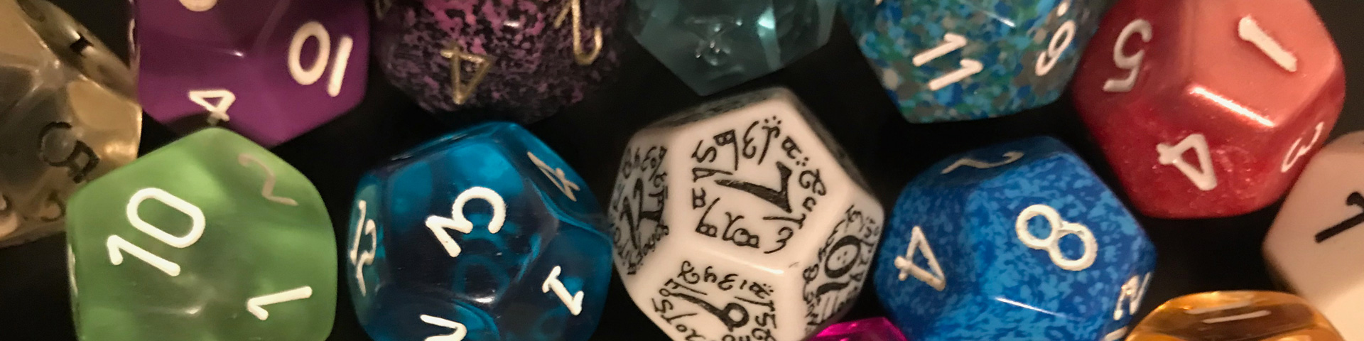 Various shades and colors of twelve-sided dice resting on a black surface.