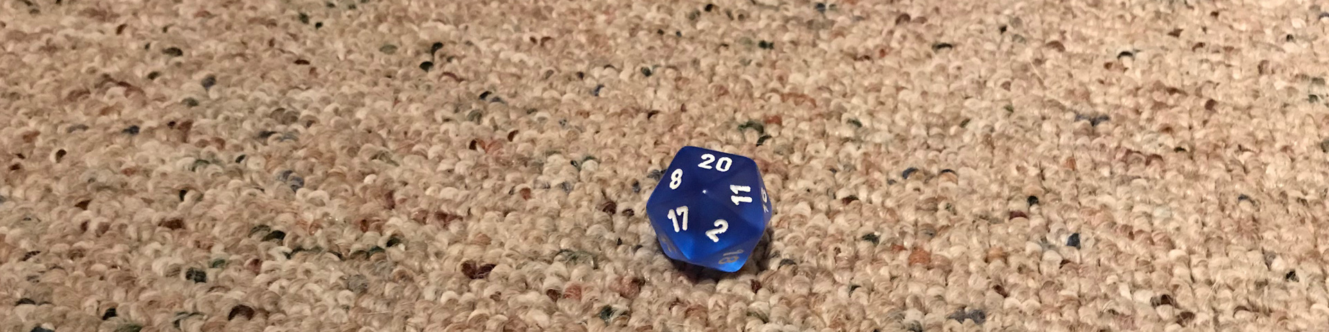 A single blue d20 rests on carpet.