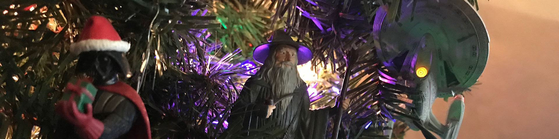 Three ornaments - Darth Vadar, the wizard Gandalf, and the starship Enterprise - appear on a Christmas tree.