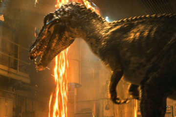 A bipedal dinosaur appears in a burning building, threatening a man and a woman who appear off to the left.
