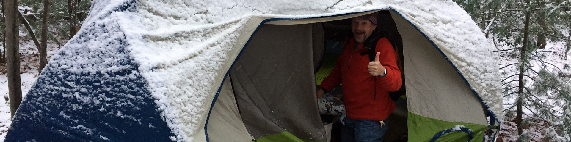 A middle-aged man (Ken Newquist) gives the thumbs up from a snow covered tent