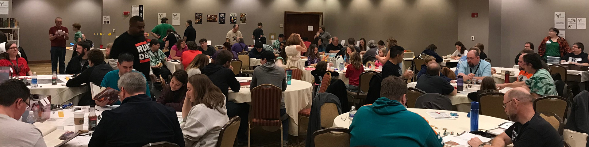 A large conference room at a game convention, with many people playing games at round tables.