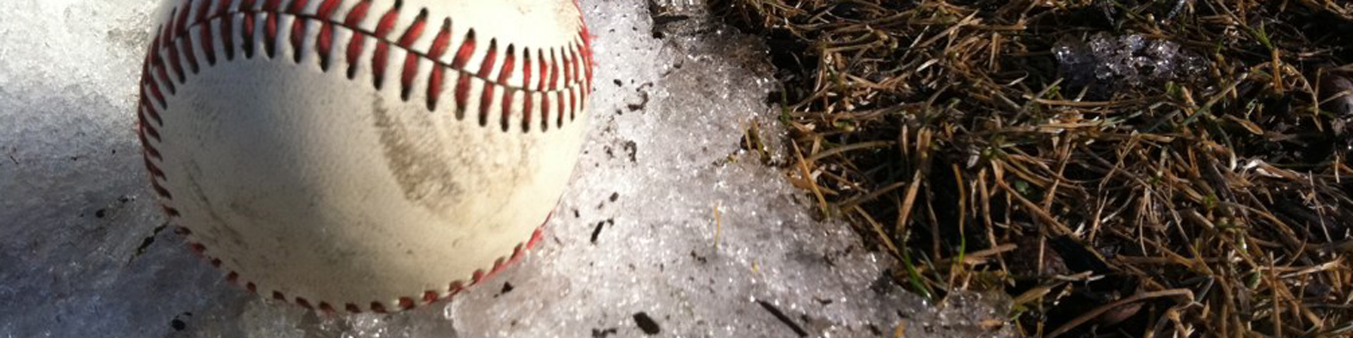 A baseball sitting on snow next to a bare spot of ground.