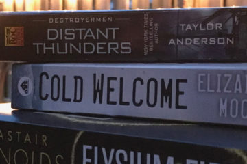 A stack of three books, with a small garden and white string lights in the background.