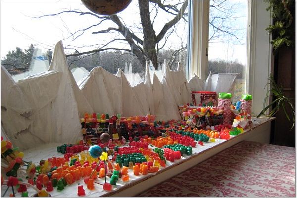 The forces of good and evil (represented as small candies) battle upon a table top. White mountains appear in the background.