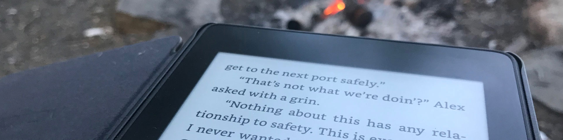 A Kindle e-reader open to text in the foreground, with a campfire in the background.