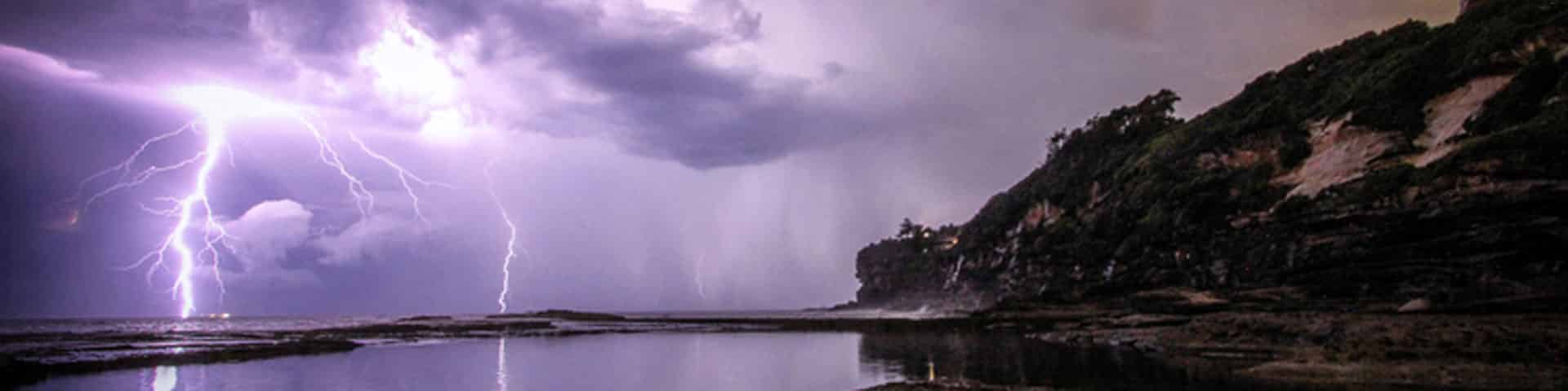 An example of weather in RPGs - lightning strikes down from clouds over the ocean. Darkened land can be seen to the right.