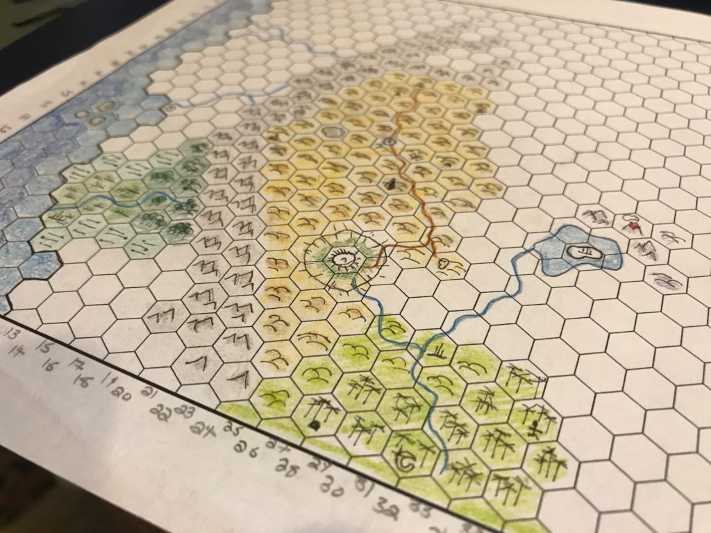 Hex paper with the beginnings of a map on it. Mountains are brown. Hills are yellow shading to green near the bottom of the map. An ocean is visible on the left side of the map.