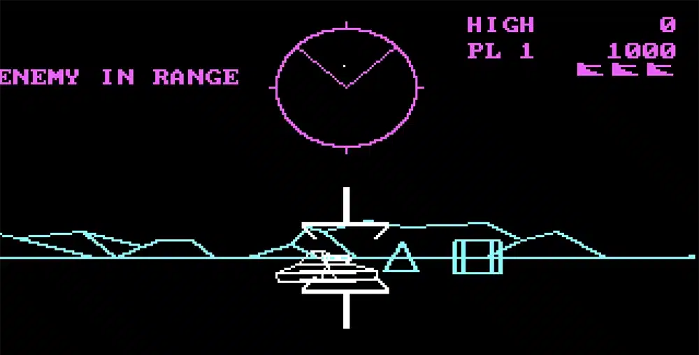 The heads up display in Battlezone. A white tank appears in the middle of the screen, along with a targeting bracket. Blue, vector-drawn mountains appear in the background. The text ENEMY IN RANGE appears in pink in the upper left hand corner of the screen. In the center of the screen is a circular radar section depicting the location of enemies. The high score, current score, and number of lives remaining appears in the upper righthand corner.